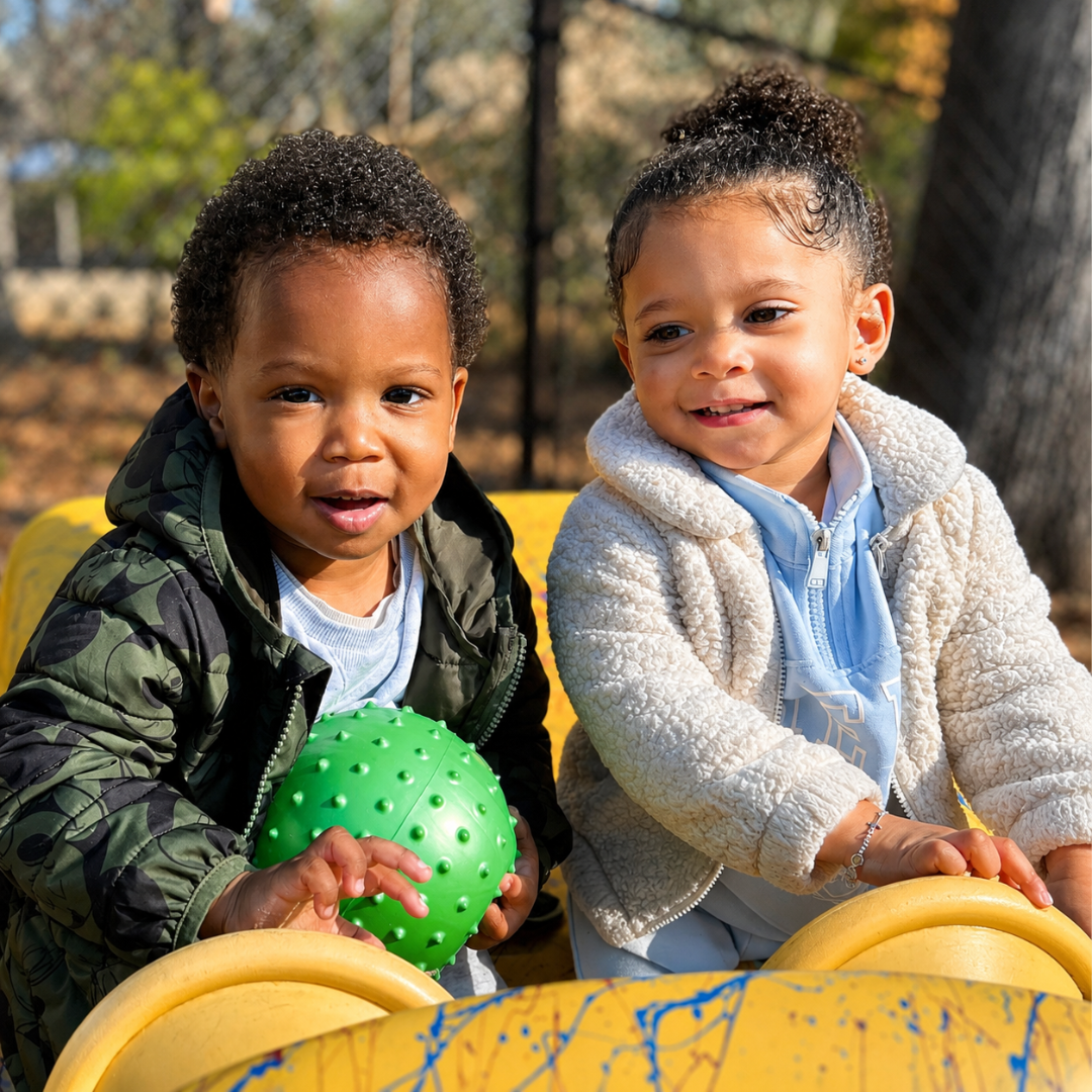 Two older toddler friends smiling together on the playground